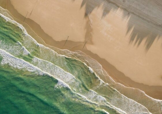 Luftfoto af bølger, sandstrand og mørke strømspor i havet