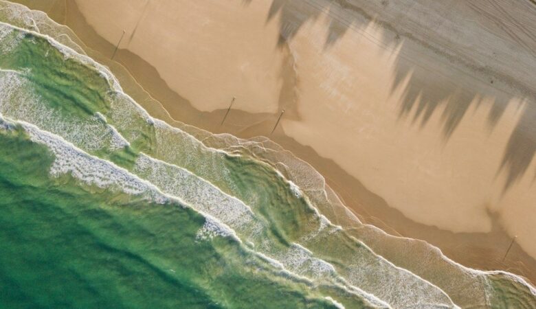 Luftfoto af bølger, sandstrand og mørke strømspor i havet